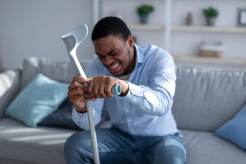 man injured sitting on couch with cane walker